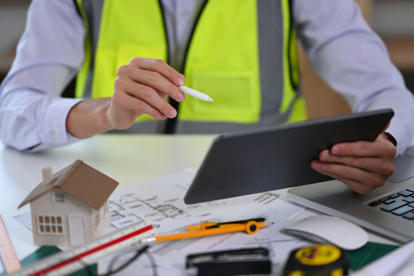 Ingeniero revisando un diseño en una tableta sobre planos y una maqueta